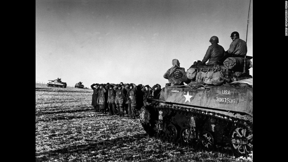 American troops ride on a tank while German POWs are held nearby.