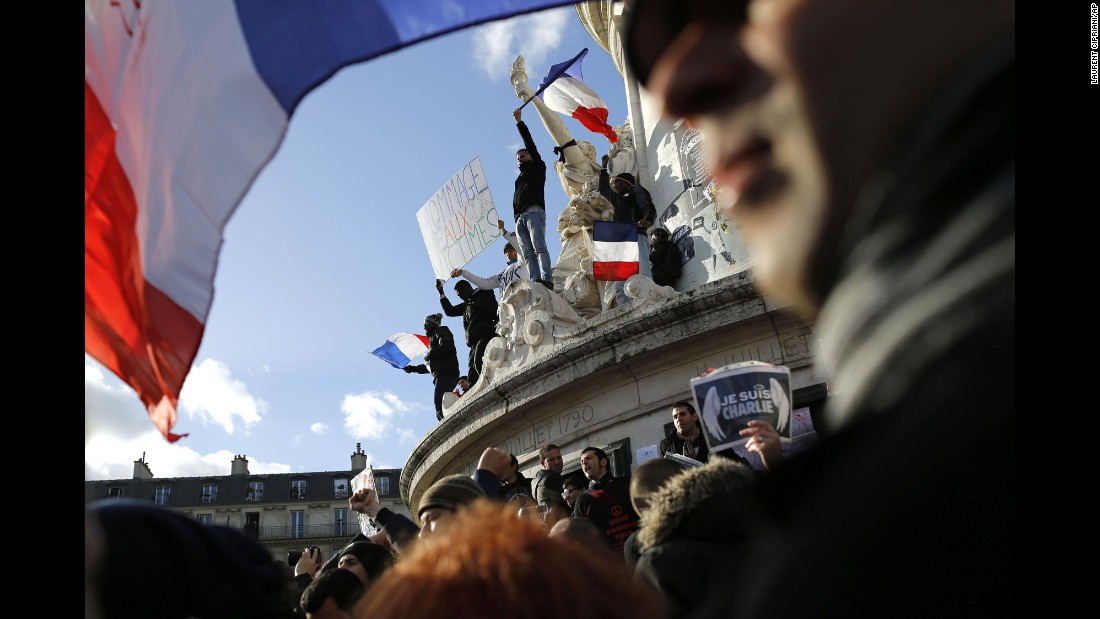 Demonstrators wave flags on the monument at the center of the Place de la Republique before the rally.