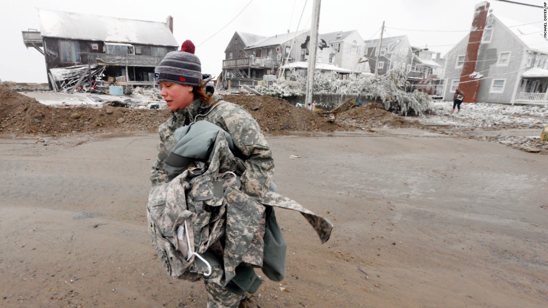 U.S. Army soldier Jennifer Bruno carries belongings from her house, center rear, which was heavily damaged by storm surge in Marshfield, Massachusetts.
