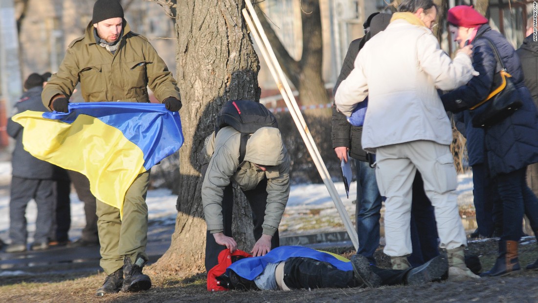 A man holds a Ukrainian flag as he covers a victim of an explosion in Kharkiv, Ukraine, on Sunday, February 22. The explosion during a peaceful protest left two dead and 15 wounded. 