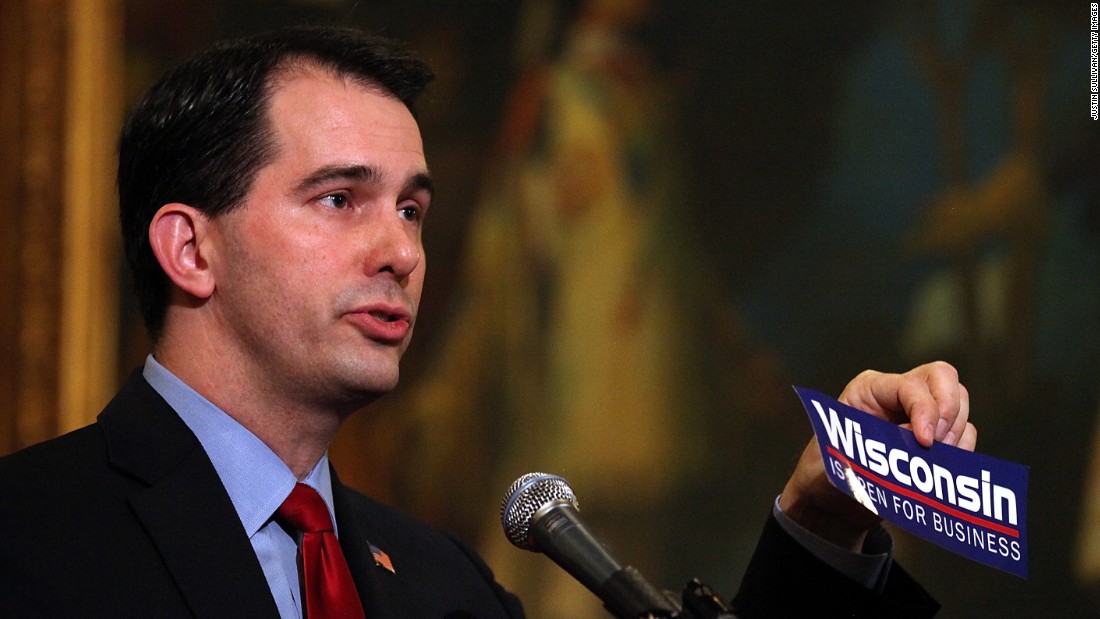 Walker holds up a &#39;Wisconsin is open for business&#39; bumper sticker as he speaks during a ceremonial bill signing outside his office at the Wisconsin State Capitol on March 11, 2011, in Madison, Wisconsin. 