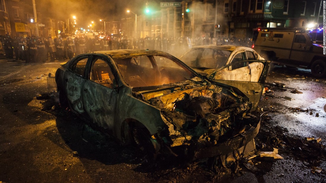 Police retreat from burned-out cars in an intersection on Monday, April 27.