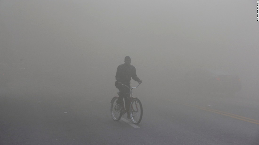 A man rides a bicycle through heavy smoke emitting from a nearby store on fire April 27.