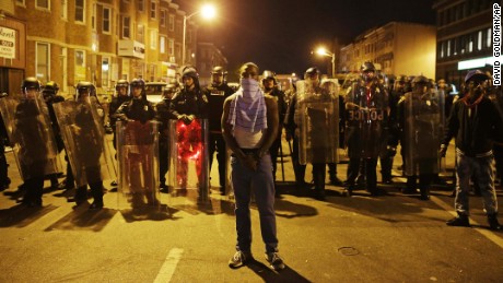 A man stands in front of a line of police officers in riot gear as part of a community effort to disperse the crowd ahead of a 10 p.m. curfew in the wake of Monday&#39;s riots following the funeral for Freddie Gray, Tuesday, April 28, 2015, in Baltimore. (AP Photo/David Goldman)