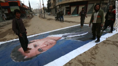 Fighters from a coalition of Islamist forces stand on a huge portrait of Syrian President Bashar al-Assad on March 29, 2015, in the Syrian city of Idlib, the second provincial capital to fall from government control.