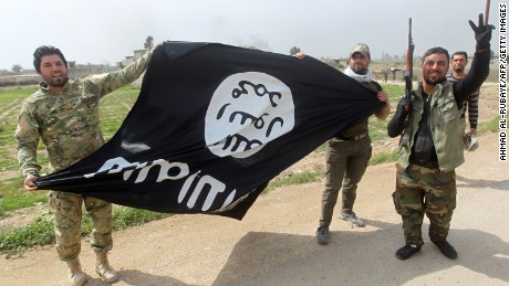 Members of Iraqi paramilitary Popular Mobilisation units, which are dominated by Shiite militias, celebrate with a flag of the Islamic State (IS) group after retaking the village of Albu Ajil, near the city of Tikrit, from the jihadist group, on March 9, 2015.