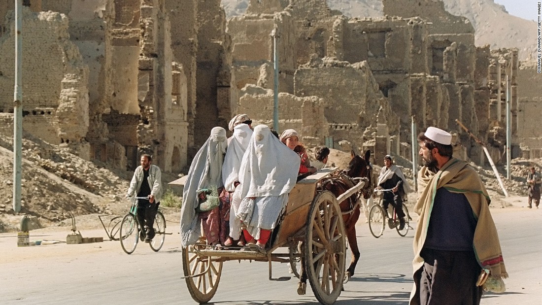 Three women hitch a ride on the back of a donkey cart as they pass by the ruins of Kabul&#39;s former commercial district in November 1996.