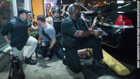 Police take cover as a barrage of gunfire erupts during a demonstration to mark the one-year anniversary of the shooting of Michael Brown on August 9, 2015, in Ferguson, Missouri. 