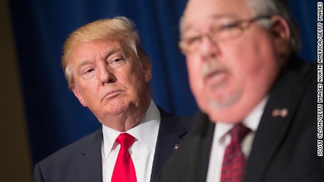 Republican presidential candidate Donald Trump listens as Sam Clovis speaks at a press conference at the Grand River Center on August 25, 2015 in Dubuque, Iowa. Clovis recently quit his position as Iowa campaign chairman for Rick Perry.