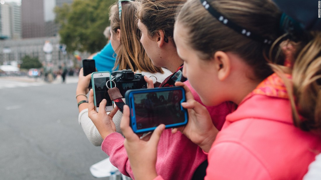 People eagerly prepare their phones to capture imagery as they wait for the Pope to pass by. 