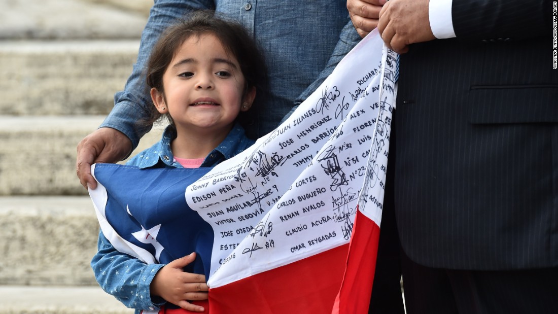 A little girl waiting for Pope Francis holds a Chilean national flag with the names of rescued miners. The men gave the Pope a signed helmet and an enlarged framed message.