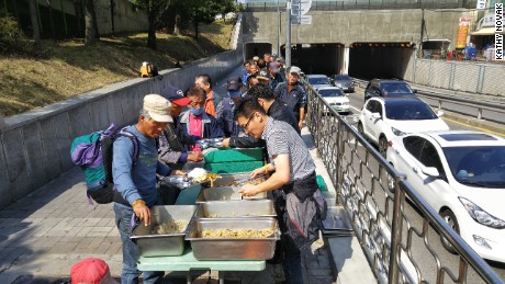 People line up to receive food from Pastor Choi Seong-Won&#39;s mobile soup kitchen.