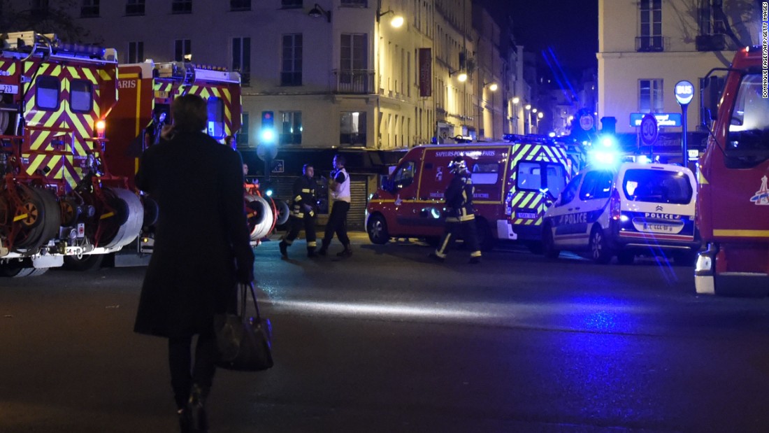 A woman walks past police and firefighters in the Oberkampf area of Paris.