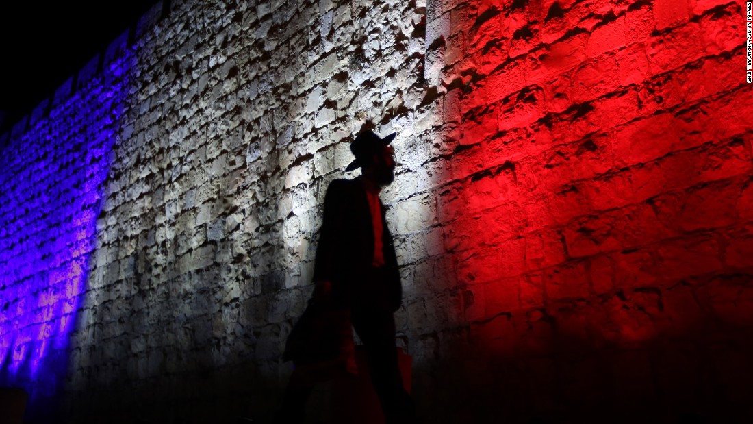 A man walks past Jerusalem&#39;s Old City walls, which were illuminated in the colors of the French flag on November 15.