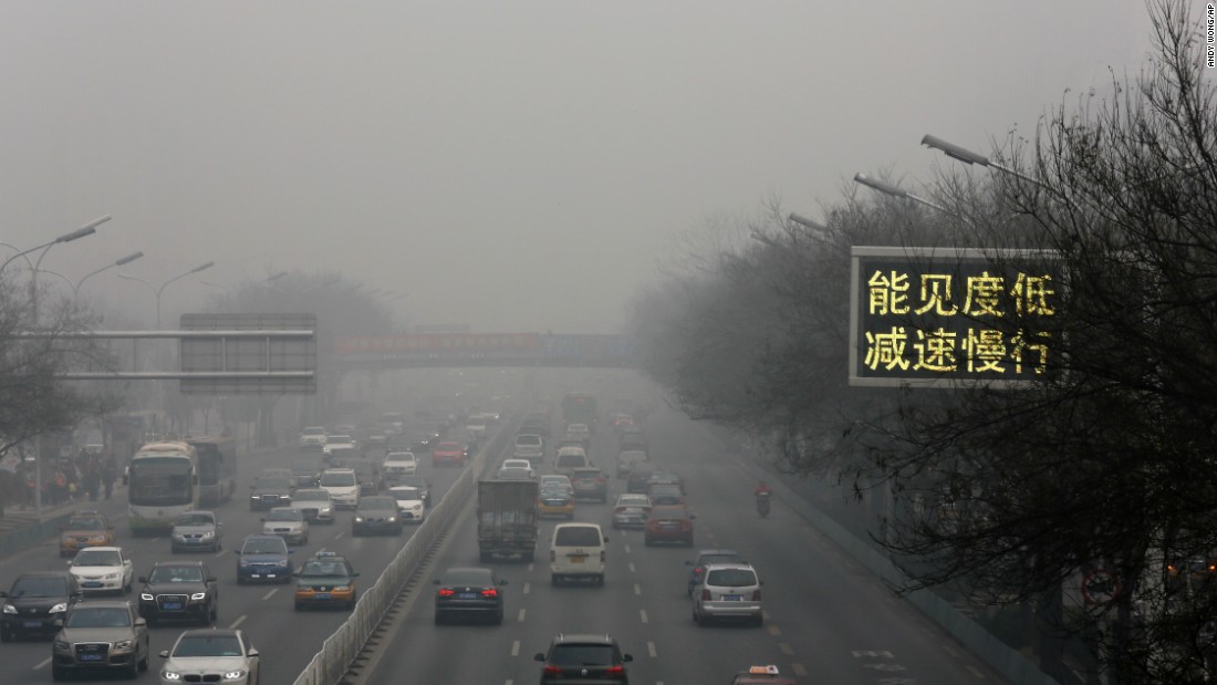 Vehicles drive along a highway in Beijing with a traffic sign that reads &quot;Slow down, low visibility&quot; on November 30.