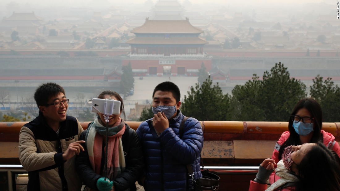 Visitors, some wearing masks to protect themselves from pollutants, share a light moment as they take a selfie at the Jingshan Park on a polluted day in Beijing on December 7, 2015, the day Beijing&#39;s city government issued its first red alert for pollution, the highest level of warning.