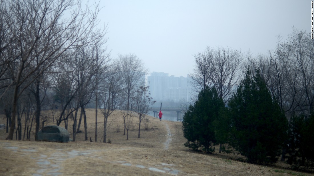 A woman walks along a path at a park in Beijing on December 7. Smog is blurring the view of the buildings in the background.