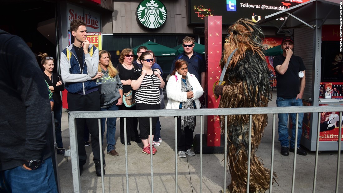 Bystanders watch as a person dressed in a Chewbacca costume walks near where fans have been congregating at the plaza in front of the TCL Theatre.