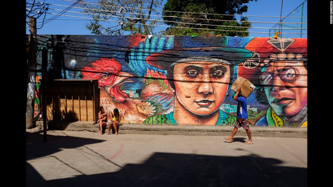 A man carries a package while two young women sit in front of a mural in Rio.