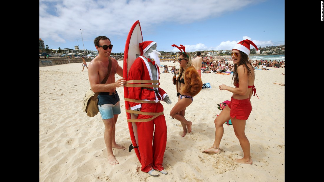 A mannequin in a Santa costume is strapped to a surfboard for easy transport along Bondi Beach as Tom Ray, left, of Britain, Ashley Pronyk of Canada, center, and Helen Maine of Britain celebrate Christmas in Sydney, Australia.