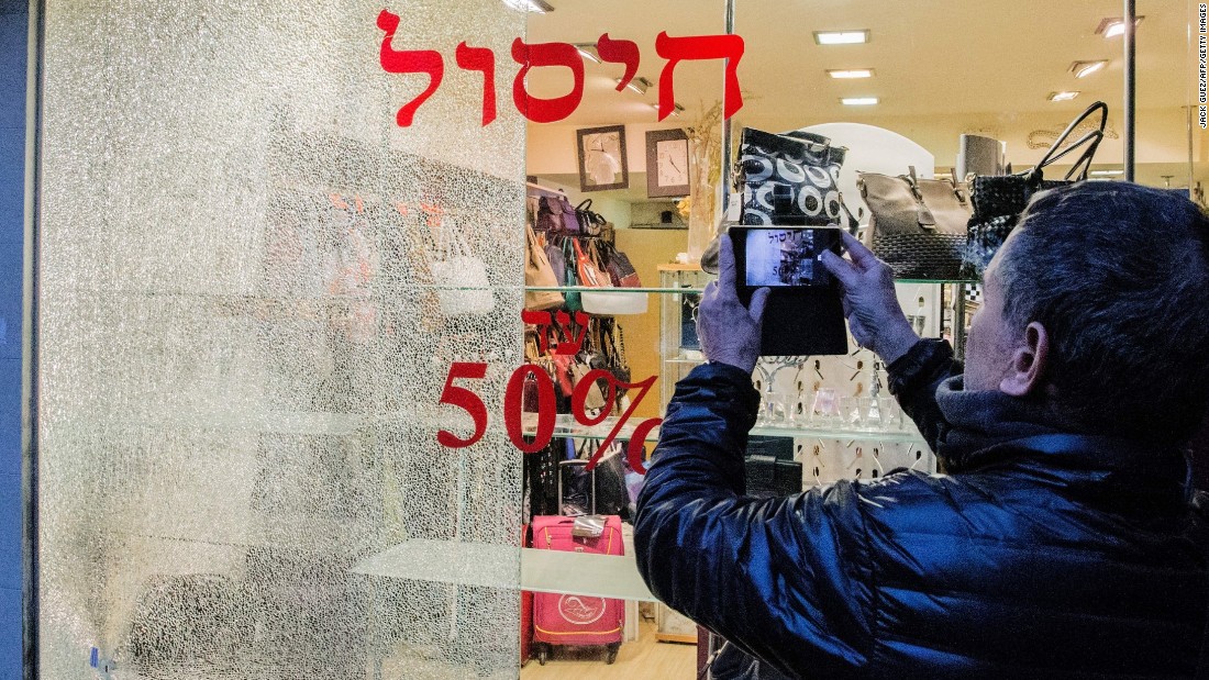 A man takes pictures of a broken shop window.