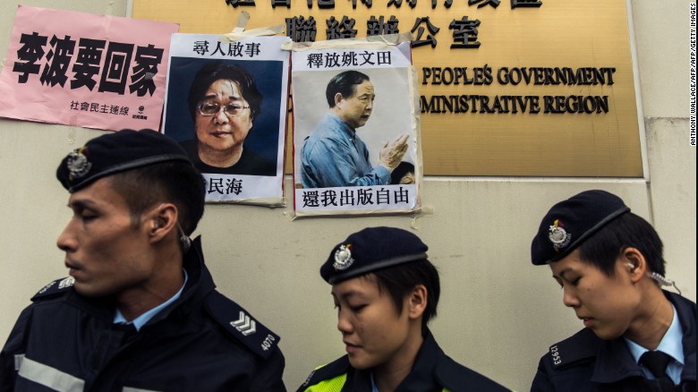 Police walk past a missing person notice of Gui Minhai (L), one of five booksellers from Hong Kong&#39;s Mighty Current publishing house who went missing in 2015.