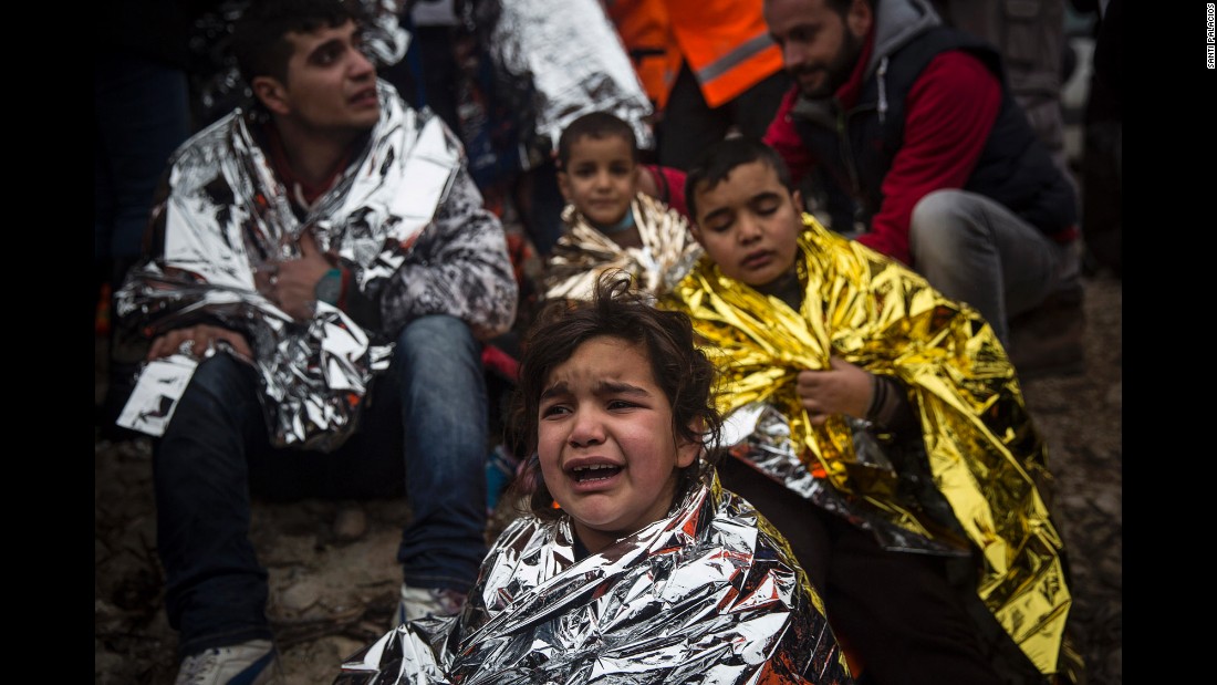 Refugees wrap themselves with thermal blankets as they sit on a beach shortly arriving on Lesbos on January 3.