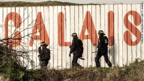 French riot police walk in front of a fence near the A16 motorway near Calais, France.