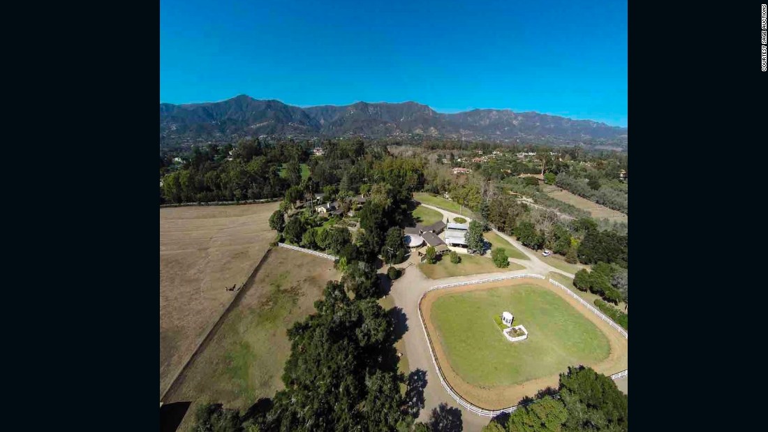 This drone aerial view shows the equestrian estate, including riding facilities, barn, and main residence, spread before the Santa Ynez Mountains.