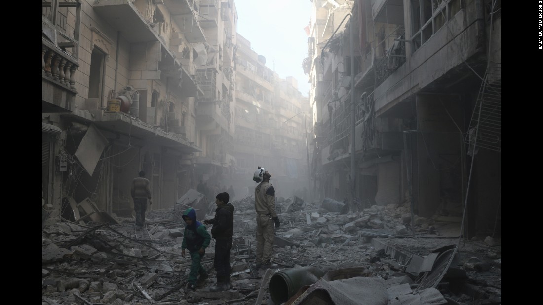 Two children walk past a &quot;White Helmet&quot; soon after an airstrike hits the Shaar neighborhood of Aleppo.