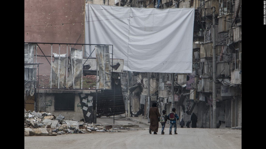 A mother watches over her children as they return from school; the massive sheet hanging in the street is to deter government snipers.