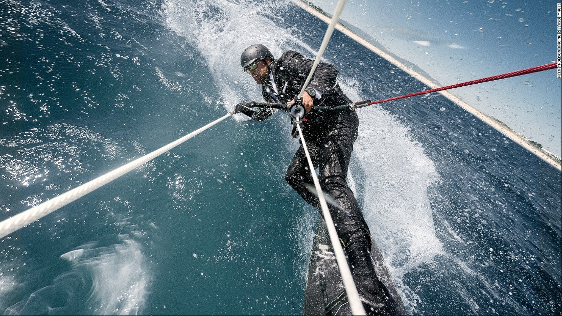Alex Thomson begins his stunt by chasing his speeding IMOCA Open 60 yacht on a kiteboard, while dressed in a sharp suit and tie.