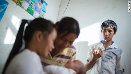 Ming sostiene un sacaleches mientras observa cómo su mujer, Cai, y su madre cuidan de su hijo recién nacido. 