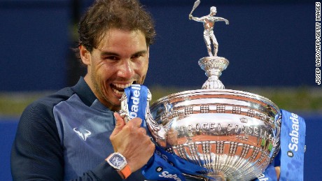 Rafael Nadal takes his customary bite out of the Barcelona Open trophy after regaining it from Japan&#39;s Kei Nishikori.