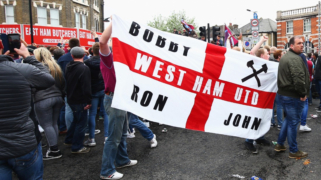 West Ham fans display a flag honoring three of the club&#39;s greatest names: former captain Bobby Moore and ex-managers Ron Greenwood and John Lyall.