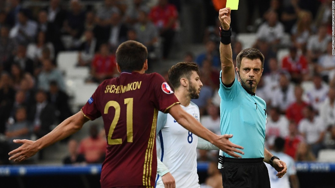Italian referee Nicola Rizzoli presents Russia defender Georgi Shchenniko, left, with a yellow card.
