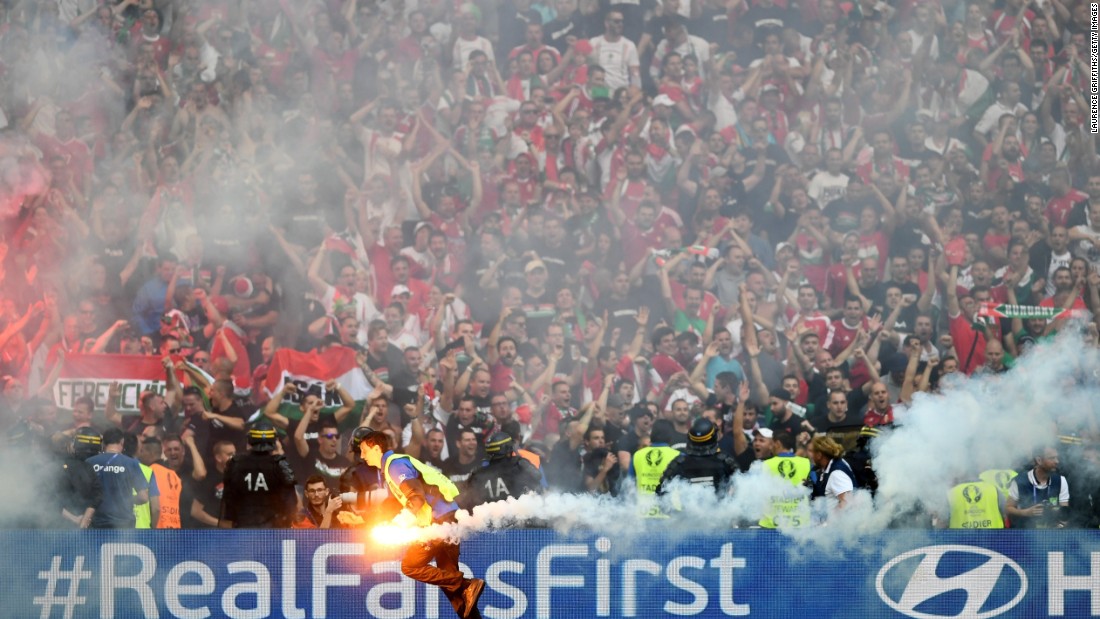 A steward picks up a flare which was thrown onto the pitch by fans.