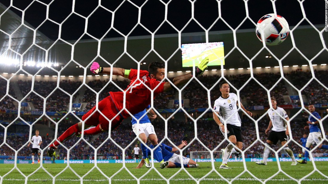 The ball flies past Gianluigi Buffon of Italy as he tries to block Mesut Oezil&#39;s opening goal.