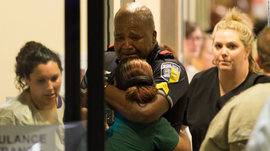 A police officer with Dallas Area Rapid Transit is comforted at the emergency room entrance of the hospital.