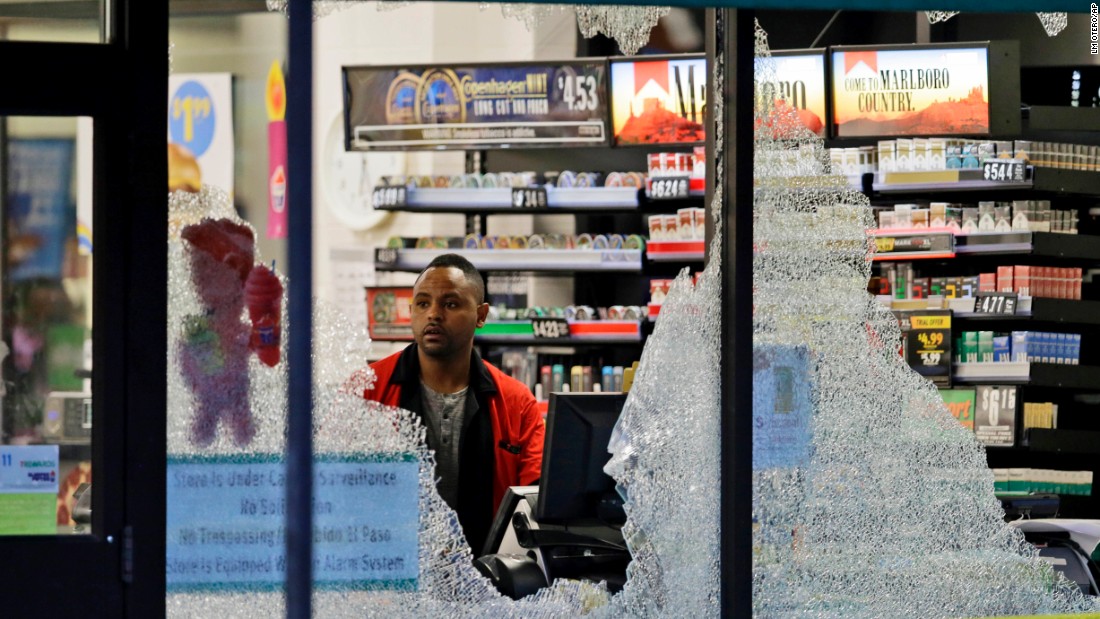 A clerk looks at broken windows that were shot out at a store in downtown Dallas.