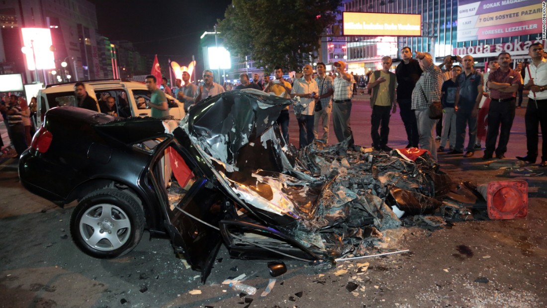 People gather around a car damaged by a tank in Kizilay Square early on July 16. 