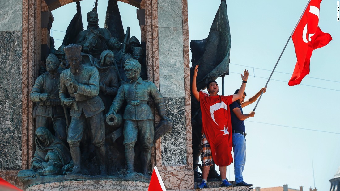 People protesting against the coup wave a Turkish flag on top of a monument in Istanbul&#39;s Taksim Square.
