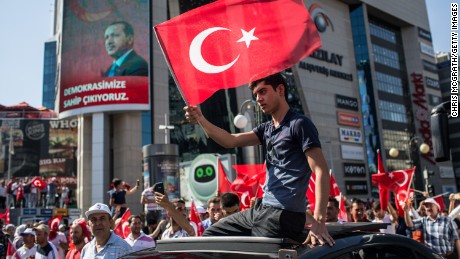 A man waves a Turkish flag from the roof of a car during a march around Ankara&#39;s Kizilay Square.