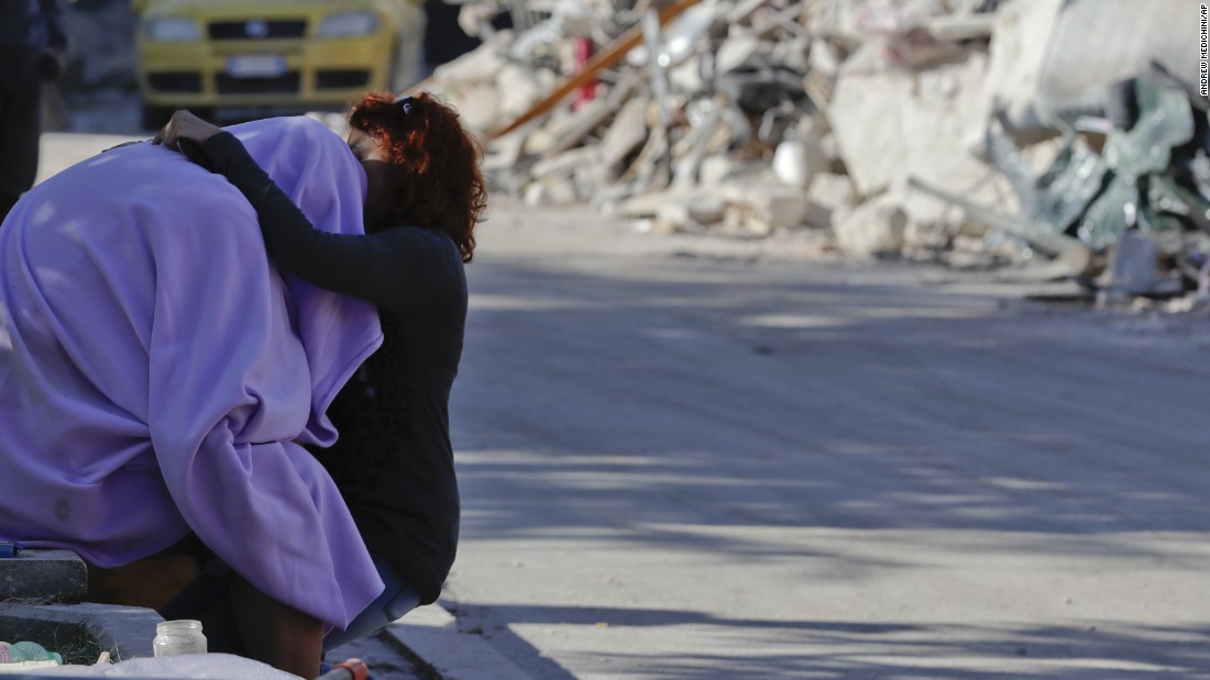 A man and woman comfort each other in front of a collapsed house in Amatrice on August 26.