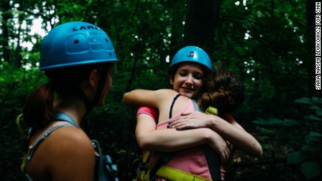 Zoe Jacobs is embraced by a teammate after climbing to the top of a tall log with a rotating platform at the top.