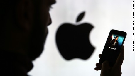 A man checks the Apple Music streaming site using his Apple Inc. iPhone 6s as he stands framed against a wall bearing the Apple logo in this arranged photograph in London, U.K., on Wednesday, Dec. 23, 2015. Beatles songs will now be available around the world on nine streaming services including Apple, Spotify, Deezer and Google Play, the bands record company, Vivendi SAs Universal Music Group, said Wednesday in a statement. Photographer: Chris Ratcliffe/Bloomberg via Getty Images