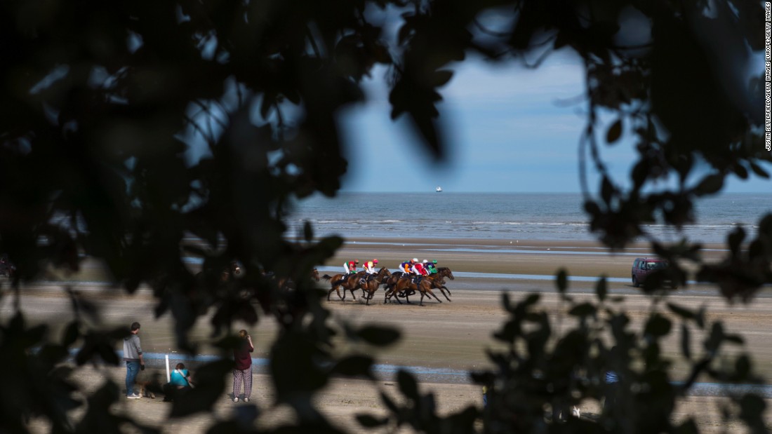 A view of the action as riders and jockeys come into view through a gap in trees above the beach.