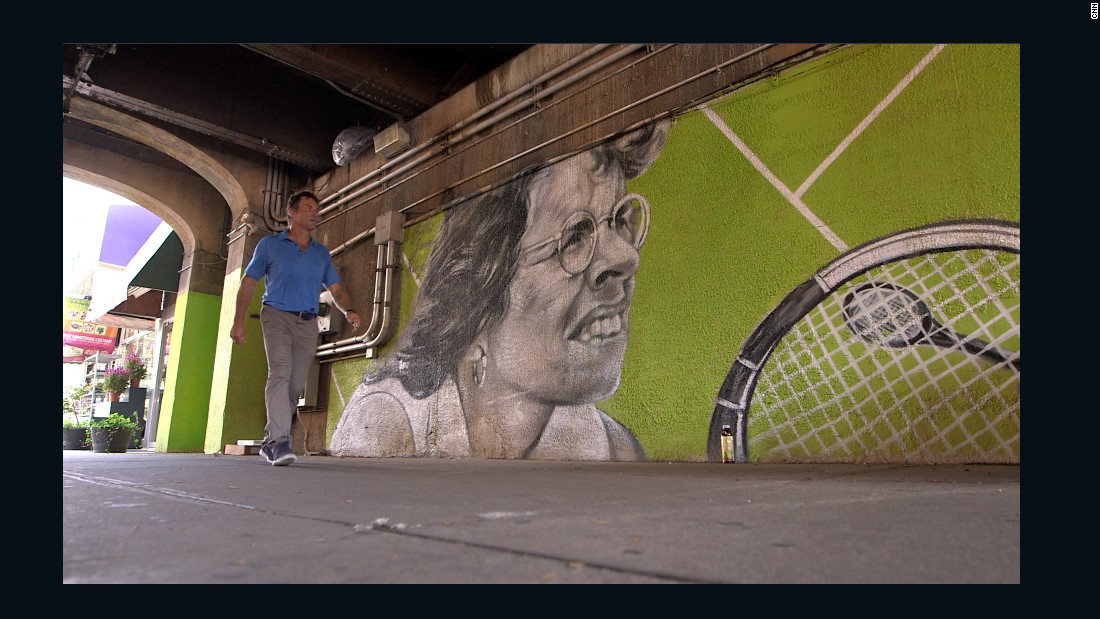 The competition was founded by Billie Jean King. Here Open Court host Pat Cash walks past a mural of the US tennis legend during CNN&#39;s visit to Forest Hills.