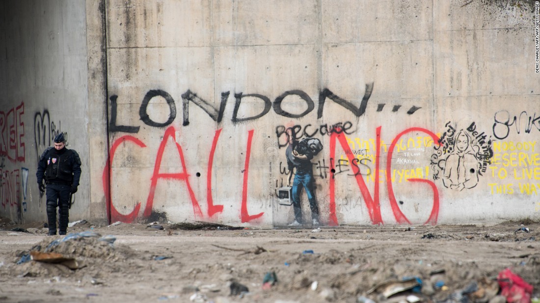 A French riot policeman stands near graffiti during the dismantling of the southern part of &quot;The Jungle&quot; migrant camp on Thursday, March 10. The graffiti reads &quot;London calling,&quot; a reference to how the camp has become notorious for migrants and refugees trying to enter the UK illegally.