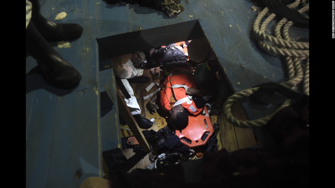 Members of Proactiva Open Arms NGO prepare to evacuate a body on a stretcher from the third level of a wooden vessel.